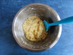Matzo ball batter in a mixing bowl, whipped egg whites folded in by blue silicone spatula, on a blue countertop.