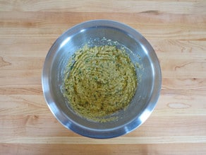 Egg and matzo meal mixed with fresh chopped dill in a stainless steel mixing bowl.