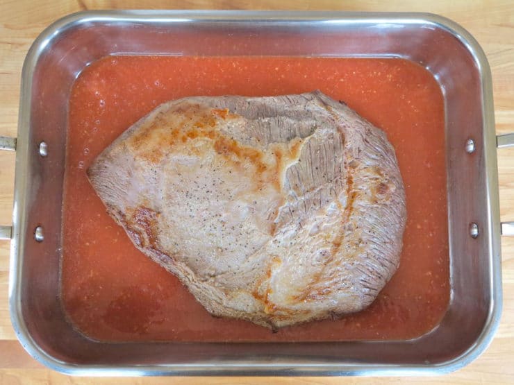 Brisket in tomato marinade in a roasting pan.