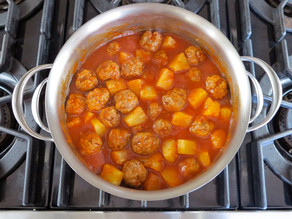 Meatballs set in stockpot of sauce.