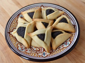 Plate of poppy seed hamantaschen on a wooden cutting board.