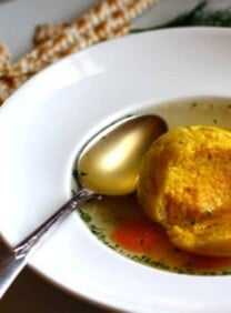 Saffron Matzo Balls soup served in a bowl with a spoon and a side of crackers on a plate