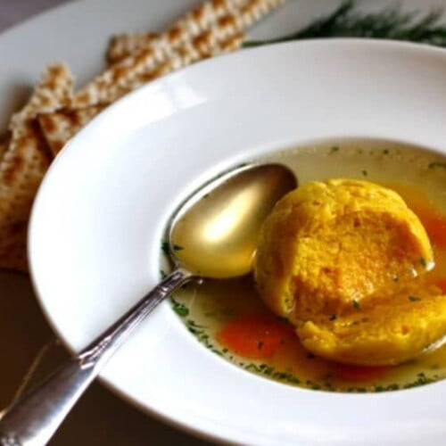 Saffron Matzo Balls soup served in a bowl with a spoon and a side of crackers on a plate