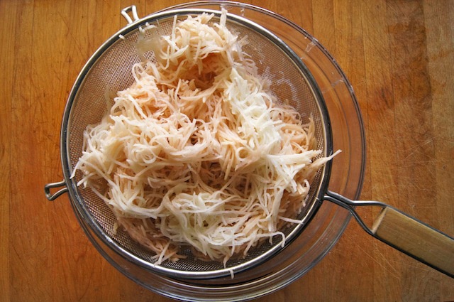 Grated potato straining over a bowl.