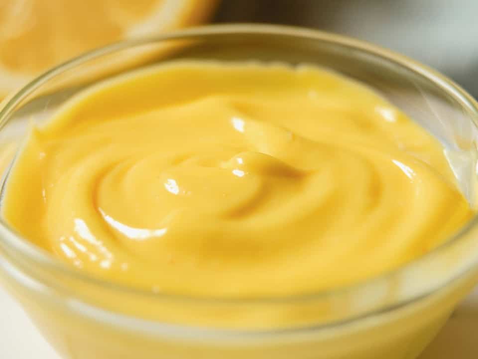 Close up - small glass dish of rich, creamy, luscious yellow hollandaise sauce, lemon half in background.