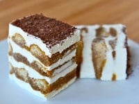 A slice of tiramisu cake with layers of coffee-soaked ladyfingers, creamy mascarpone cheese, and a dusting of cocoa powder