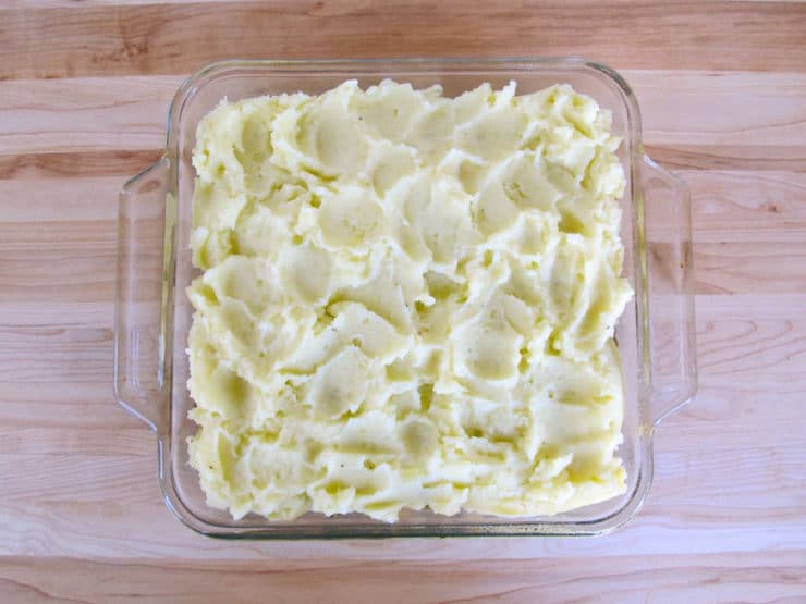 Mashed potatoes spread over vegetables in baking dish.
