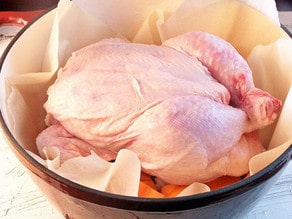 Whole chicken placed on top of vegetables in Dutch oven.