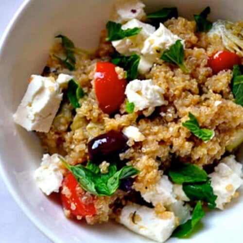 Greek Infused Quinoa Salad with tomatoes, fresh oregano, olives, and quinoa served on a white bowl