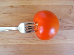 Fork spearing tomato on cutting board.