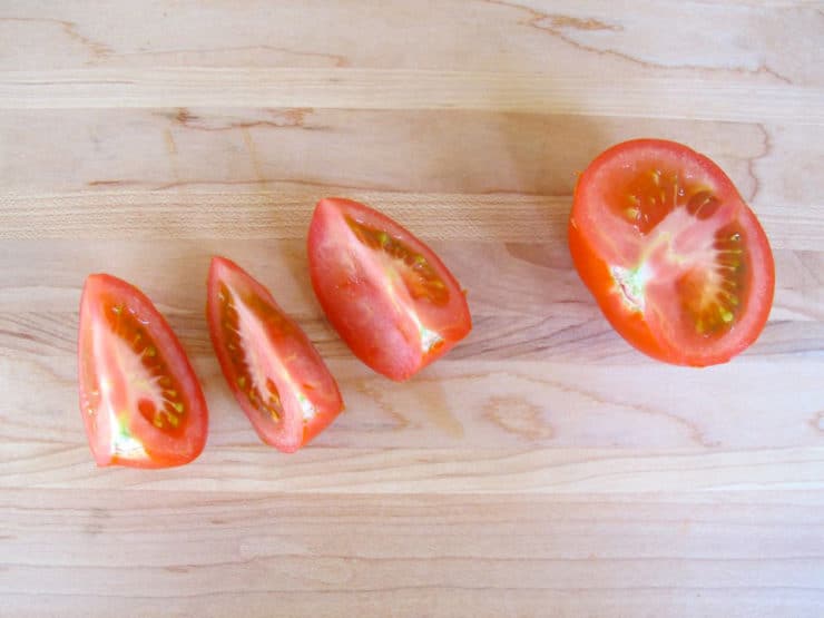 Tomato half and three tomato quarters on cutting board.