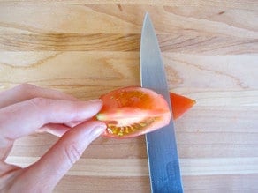 Slicing pulp and seeds from skin of tomato quarter.