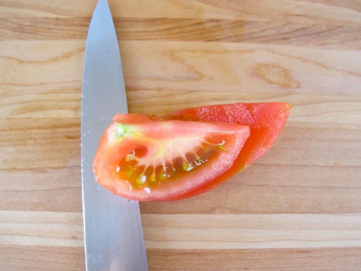 Knife removing pulp and seeds from skin of tomato quarter.