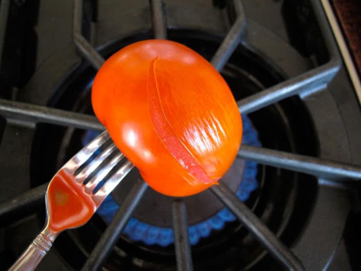 Tomato spread by fork held over gas flame on stovetop.