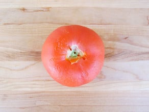 Peeled tomato on cutting board with fork holes on stem area.