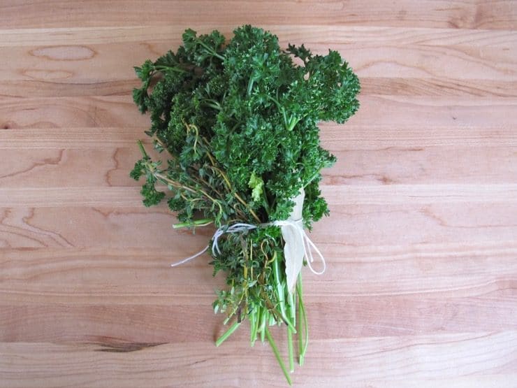 Bundle of herbs tied with string on wooden cutting board.