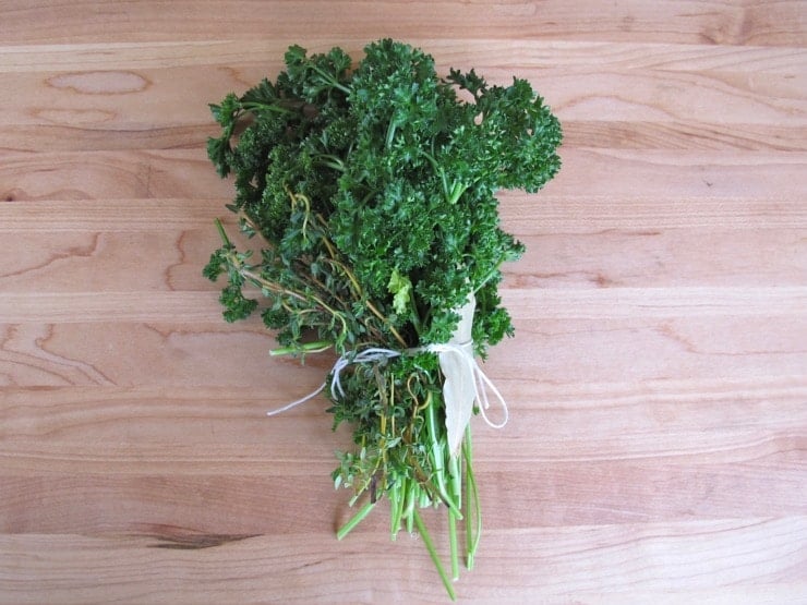 Bundle of herbs tied with string on wooden cutting board.