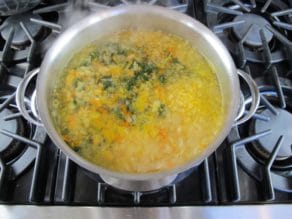 Pot of court bouillon cooking - herbs and vegetables simmering lightly in broth in pot on stovetop.