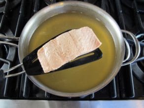 Salmon fillet poached on spatula held above a pot of Court Bouillon - Steaming hot, barely boiling, on stovetop.