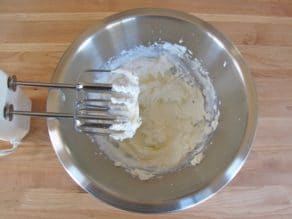 Whipping cream for Mousseline Sauce in stainless steel bowl with electric beaters on wooden background.