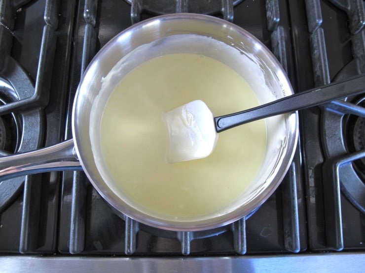 Stirring smooth sauce in pan of buttery sauce on stovetop with spatula.