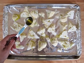 Drizzling olive oil over cauliflower florets on a baking sheet.