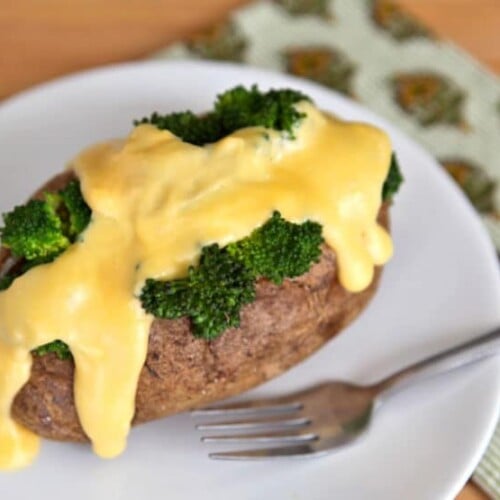 Closed of a piece of potato served with broccoli and melted cheese on top with fork on the side