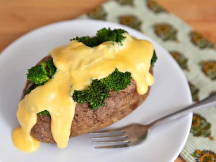 Closed of a piece of potato served with broccoli and melted cheese on top with fork on the side