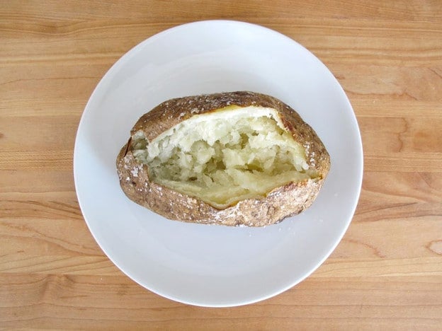 Splitting open baked potato on a plate.