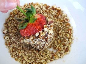 Rolling dipped strawberry in chopped nuts.