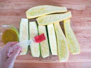 Brushing sliced zucchini with oil.