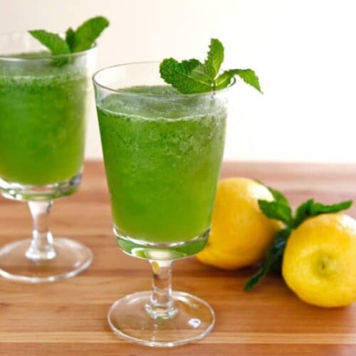 Two glasses of color green drink Limonana frozen mint lemonade with 2 lemons on the side