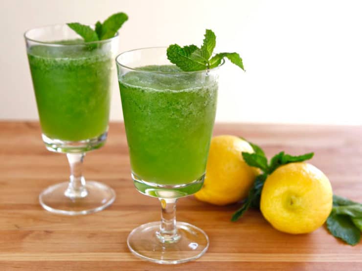 Two glasses of color green drink Limonana frozen mint lemonade with 2 lemons on the side