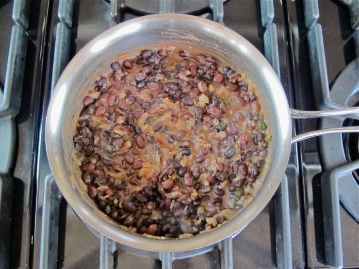 Black beans added to onions in a pot.