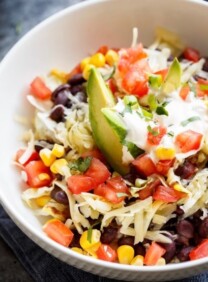 Overhead shot of Quinoa Black Bean Burrito Bowl with avocado, shredded cheese and tomatoes.