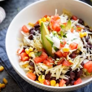 Overhead shot of Quinoa Black Bean Burrito Bowl with avocado, shredded cheese and tomatoes.