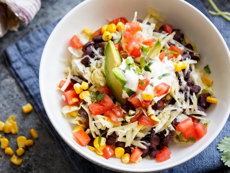 Overhead close up shot of completed Quinoa Black Bean Burrito Bowl on cloth napkin, corn scattered on the side.