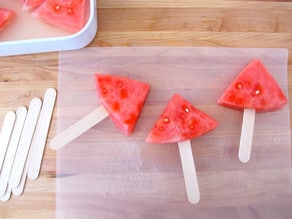 Inserting popsicle sticks into watermelon wedges.