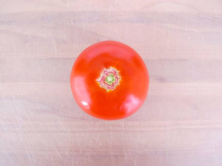 Overhead shot of whole tomato on white plastic cutting board.