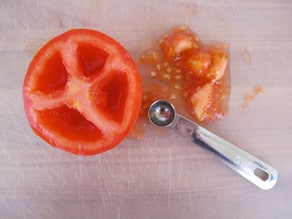 Overhead shot of tomato half with scooped out seed pulp and small metal measuring spoon.