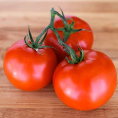 Three whole ripe red tomatoes on the vine, resting on wooden cutting board.