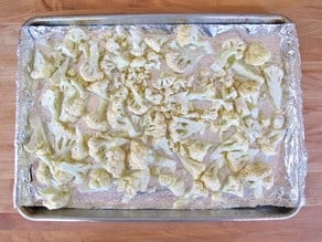 Cauliflower florets on a lined baking sheet.