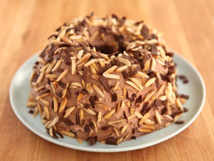 A chocolate cake with crunchy roasted nuts on top served on a white plate