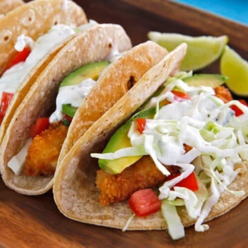 Horizontal shot of crispy panko fish tacos with sliced lemon on the sides served on a wooden tray