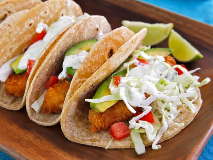 Horizontal shot of crispy panko fish tacos with sliced lemon on the sides served on a wooden tray