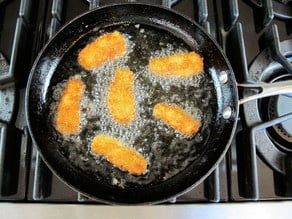 Frying fish pieces in a skillet.