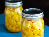 Two jars of yellow curry pickled cauliflower on a blue table