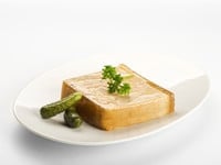 Image of a Foie Gras served on a white plate with two small pickles on side and garnished with parsley on top