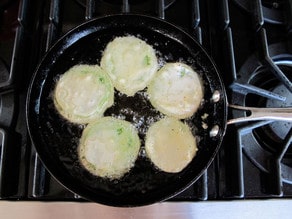 Frying green tomato slices in a skillet.