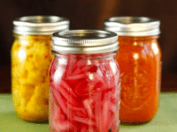 Three jars of pickled vegetables, including pickled red onions, are neatly arranged on a table
